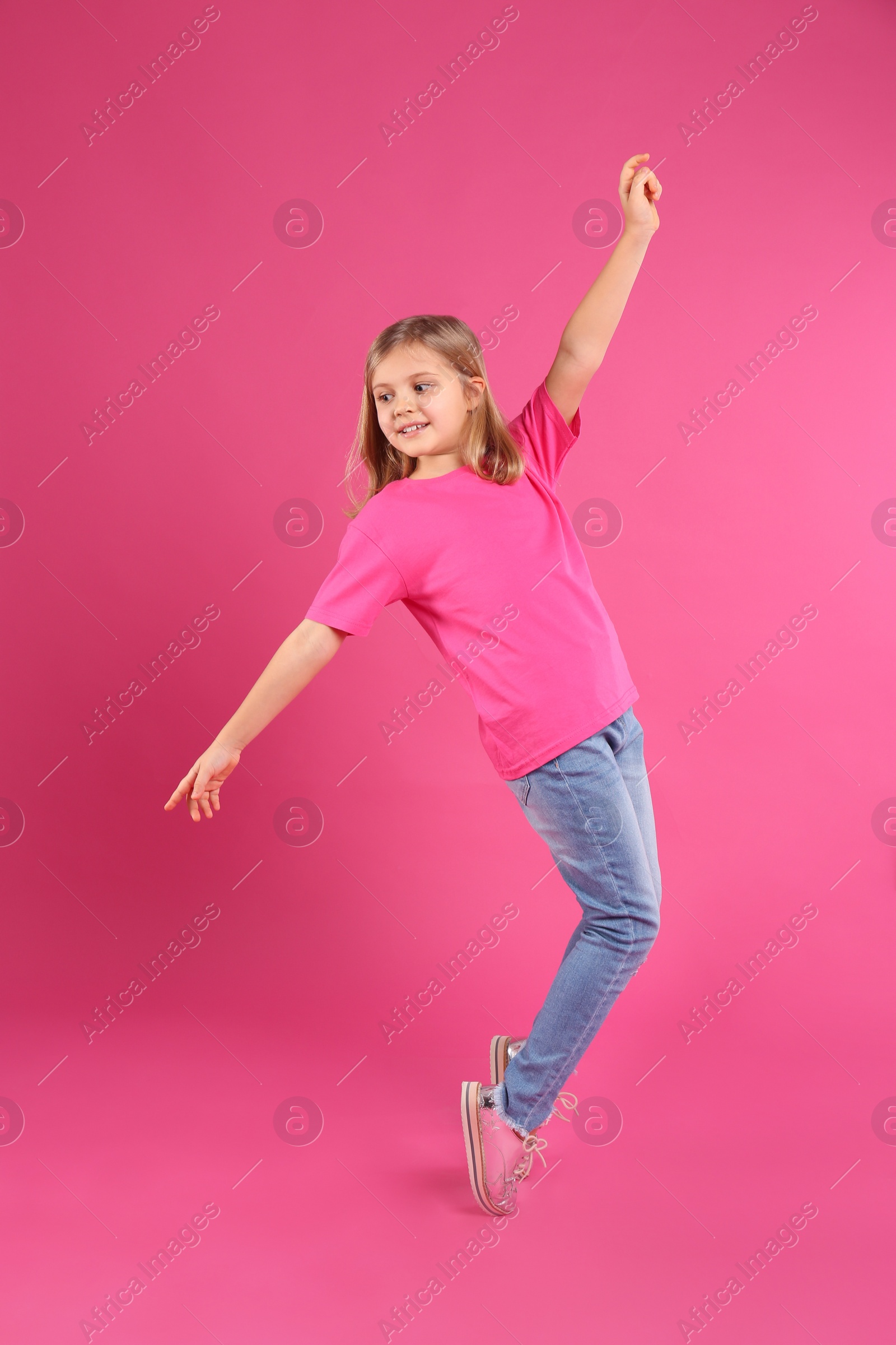 Photo of Cute little girl dancing on pink background