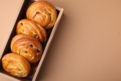 Photo of Delicious rolls with raisins in wooden box on beige table, top view and space for text. Sweet buns