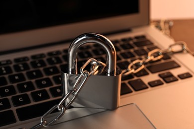 Photo of Cyber security. Laptop with padlock and chain on table, closeup