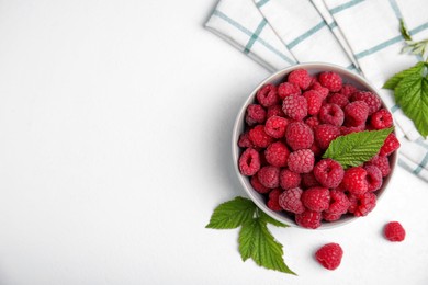 Photo of Bowl with fresh ripe raspberries and green leaves on white table, flat lay. Space for text