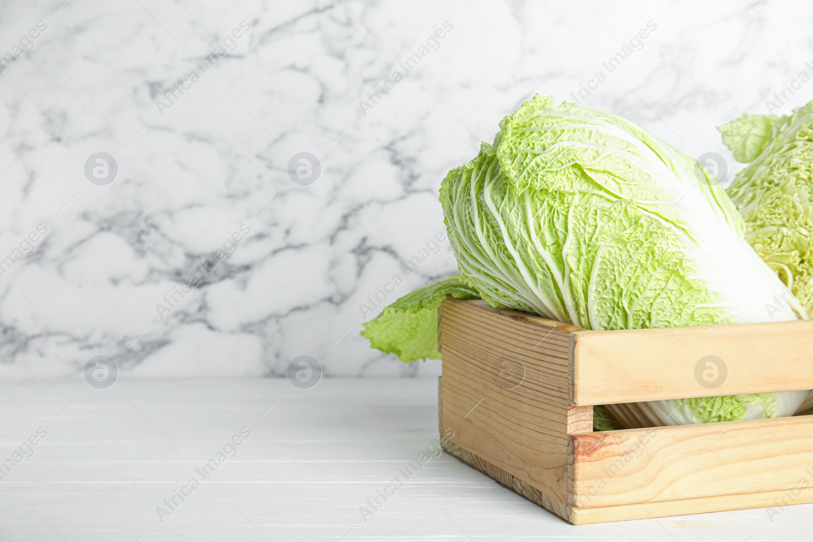 Photo of Chinese cabbages in wooden crate on white table. Space for text