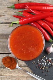 Photo of Spicy chili sauce in bowl and ingredients on wooden table, flat lay