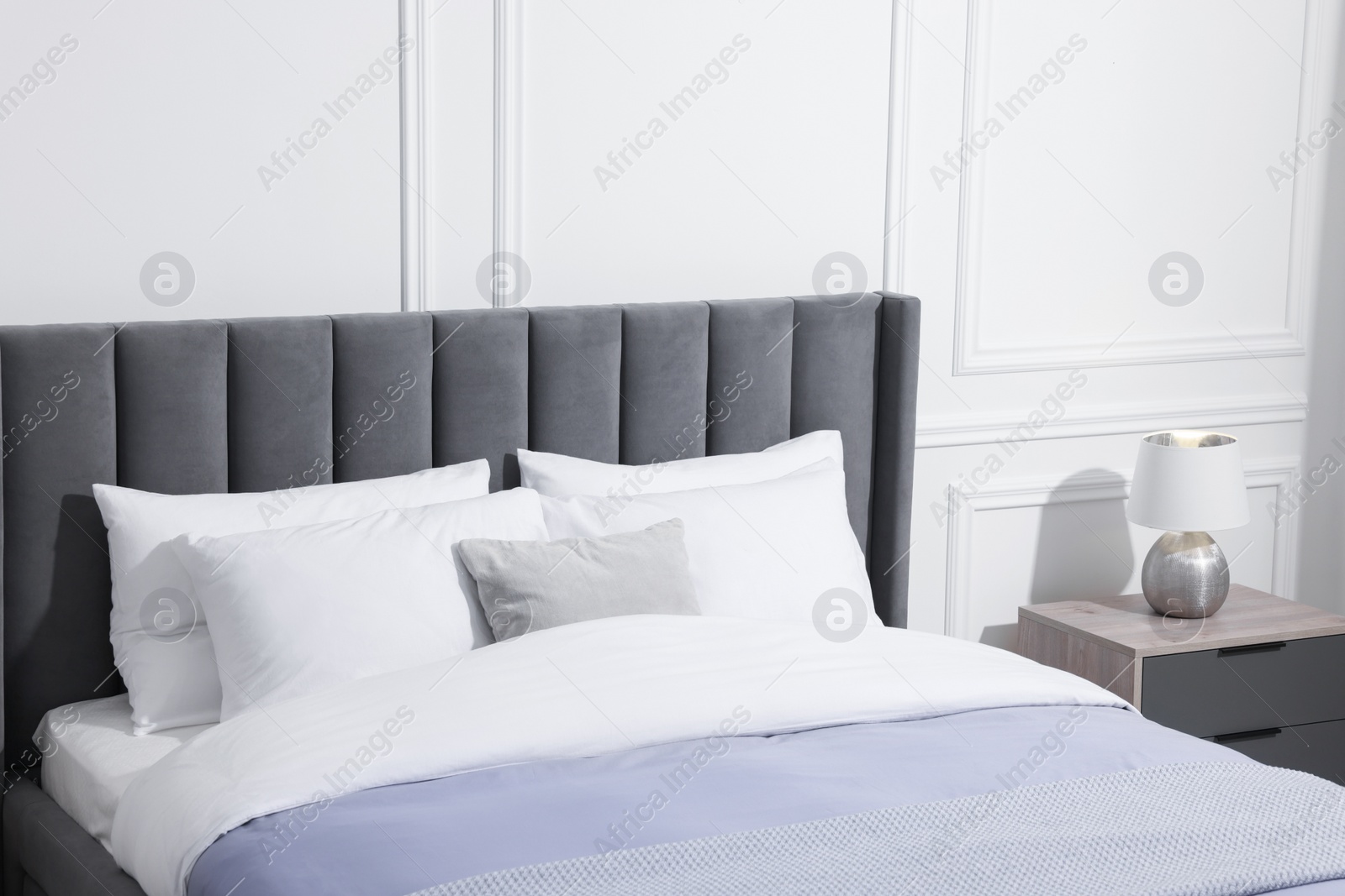 Photo of Comfortable bed near bedside table with lamp in stylish bedroom