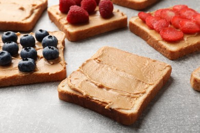 Photo of Tasty peanut butter sandwiches with fresh berries on gray table, closeup