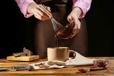 Woman pouring yummy hot chocolate into cup at wooden table, closeup