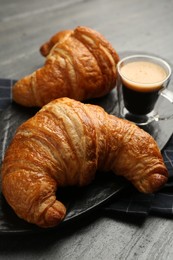 Delicious fresh croissants and cup of coffee on gray table, closeup