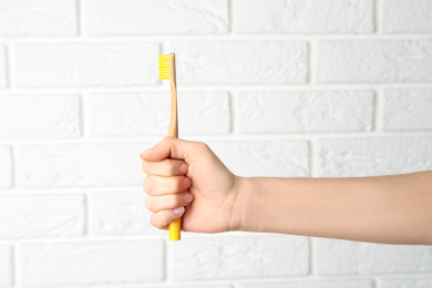 Photo of Woman holding bamboo toothbrush against white brick wall, closeup