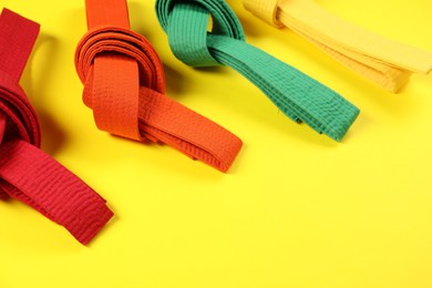 Colorful karate belts on yellow background, space for text