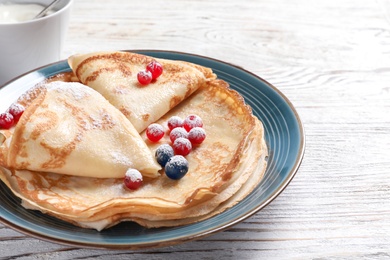 Photo of Thin pancakes served with sugar powder and berries on plate, closeup