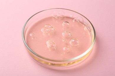 Photo of Petri dish with liquid sample on pink background, closeup