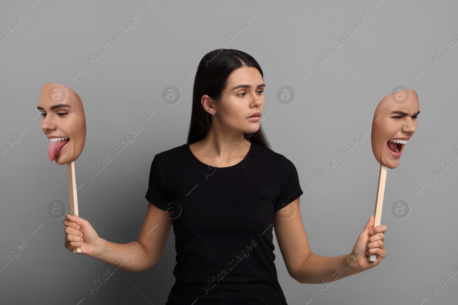 Image of Woman holding masks with her face showing different emotions on grey background. Balanced personality