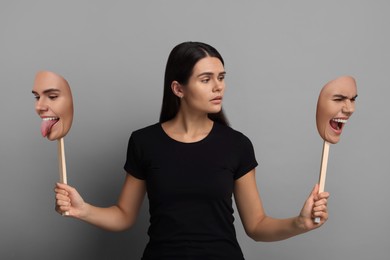 Woman holding masks with her face showing different emotions on grey background. Balanced personality