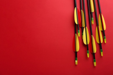 Photo of Plastic arrows on red background, flat lay with space for text. Archery sports equipment