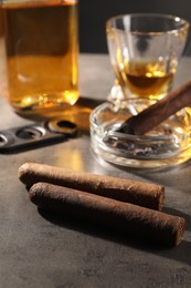 Photo of Cigars, ashtray and whiskey on grey table, closeup