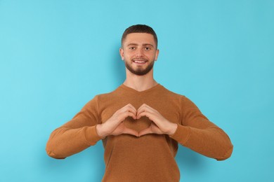 Photo of Happy volunteer making heart with his hands against light blue background