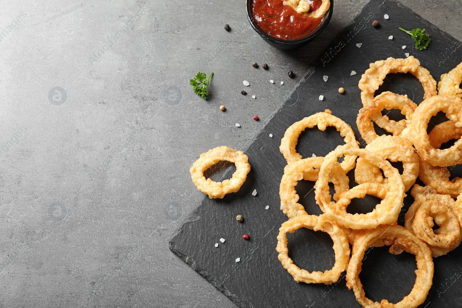 Photo of Homemade crunchy fried onion rings with tomato sauce on table, top view. Space for text