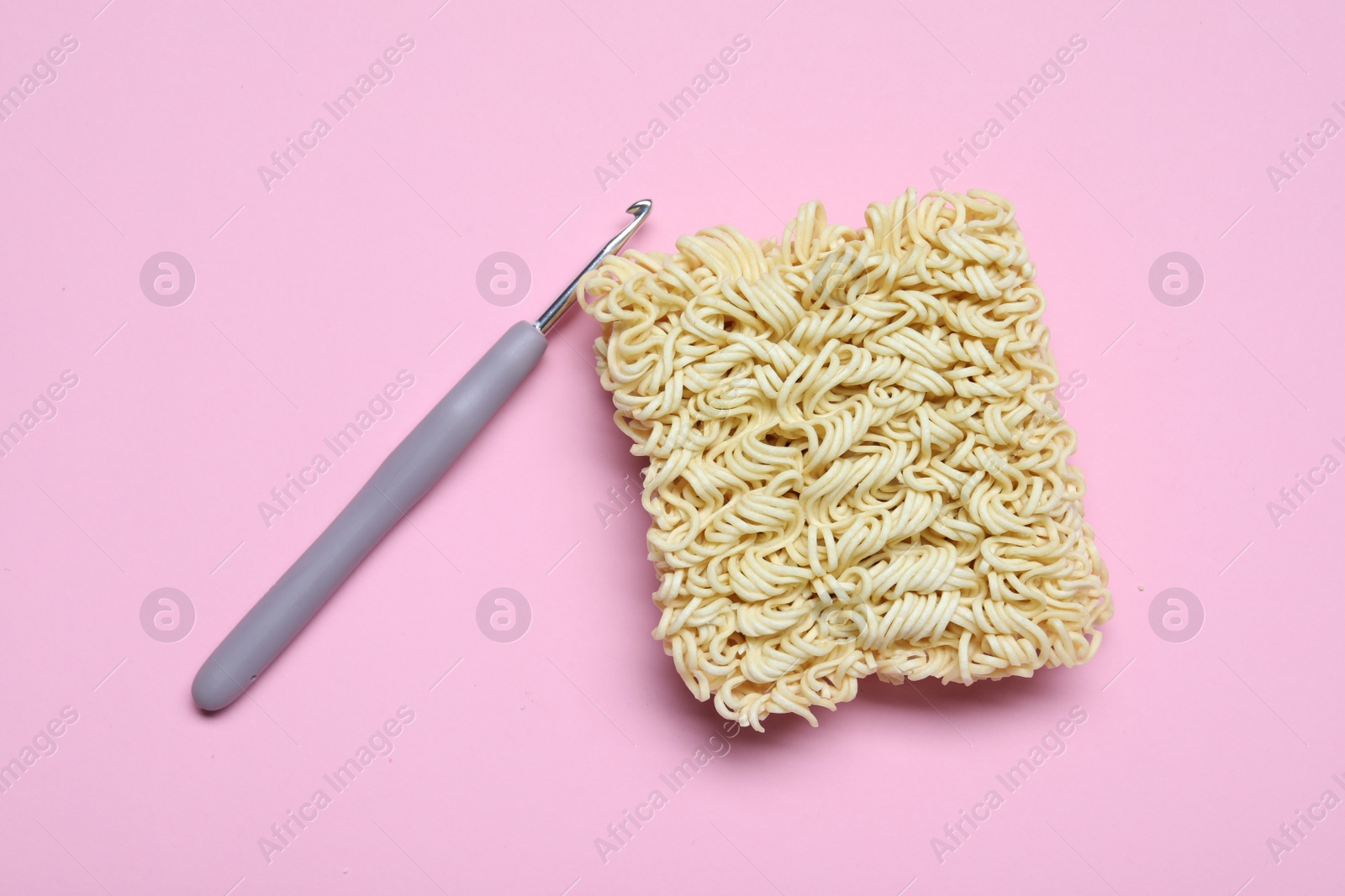 Photo of Instant noodles and crochet hook on pink background, flat lay