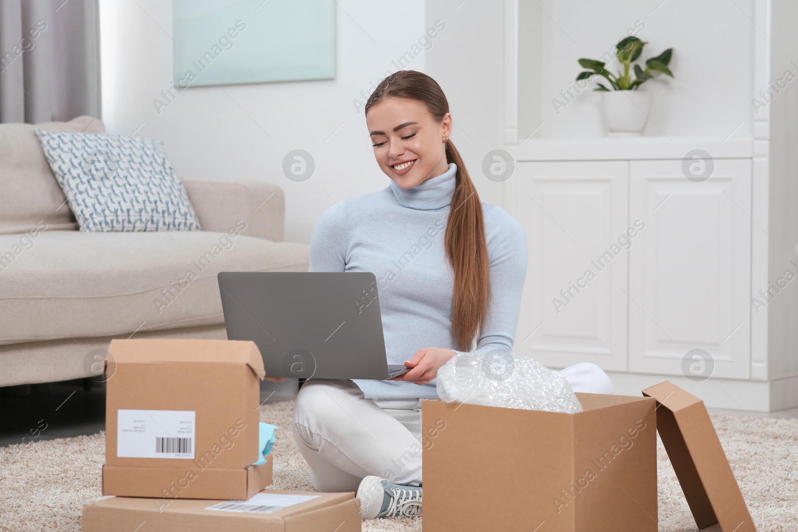 Photo of Happy woman with laptop and parcels at home. Online store