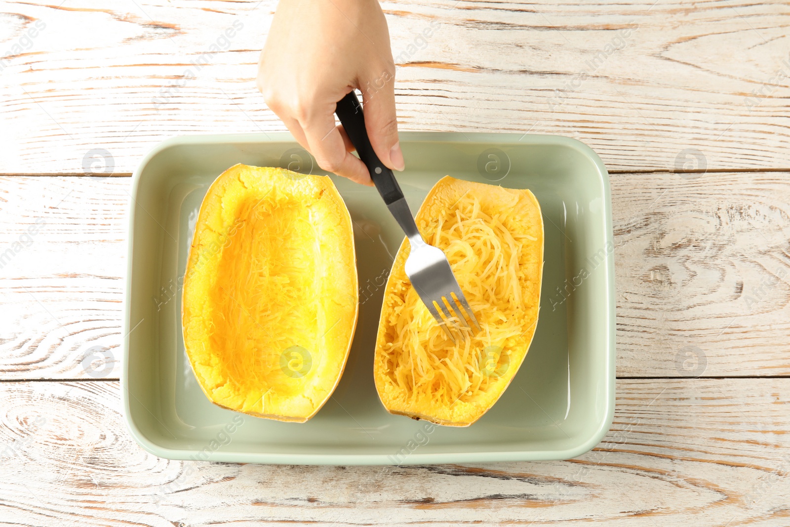 Photo of Woman scraping flesh of cooked spaghetti squash with fork on table, top view