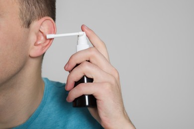 Photo of Man using ear spray on light grey background, closeup. Space for text