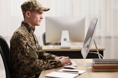 Military service. Young soldier working with computer at wooden table in office