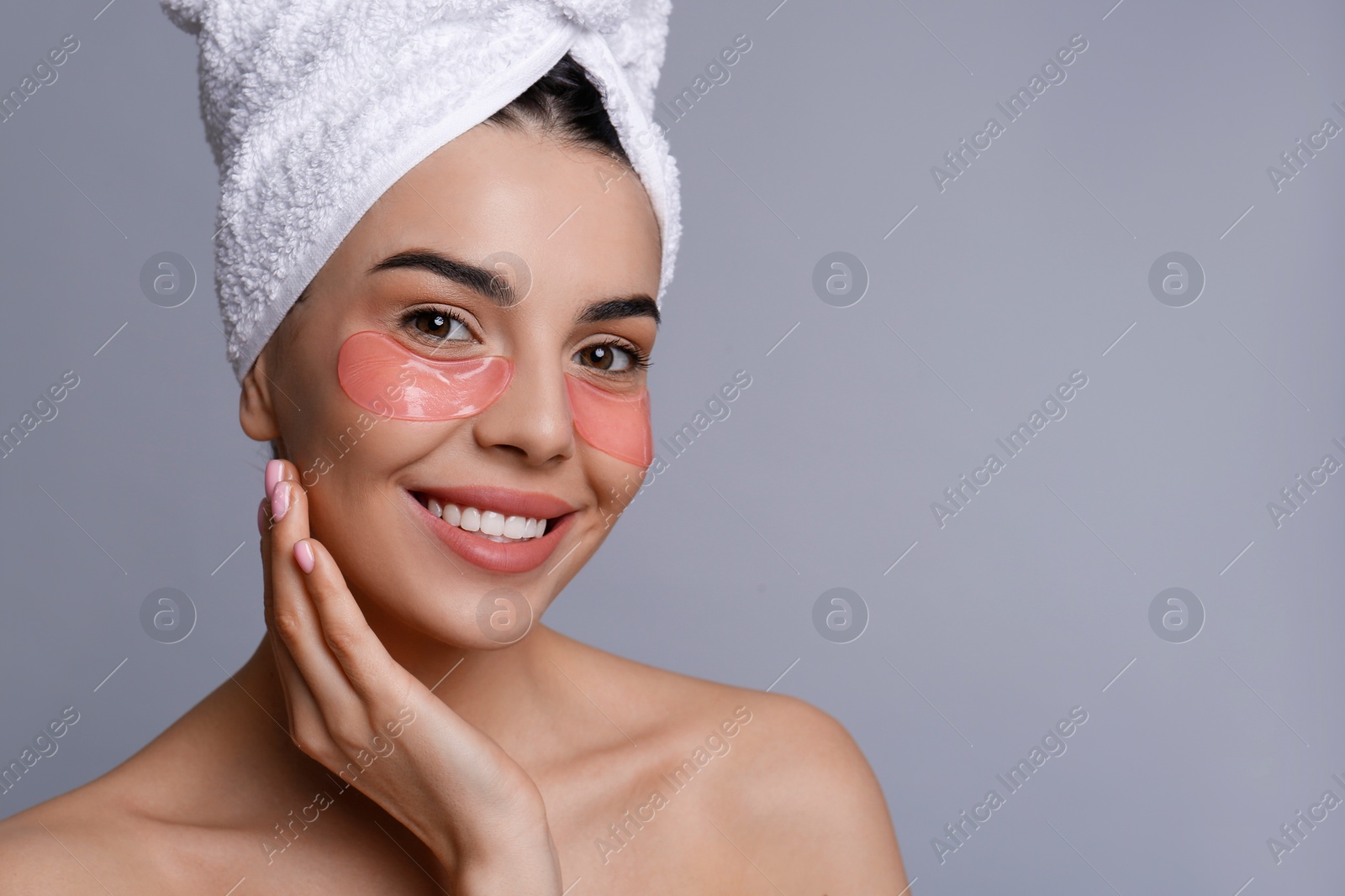 Photo of Beautiful young woman with under eye patches and hair wrapped in towel on grey background, space for text