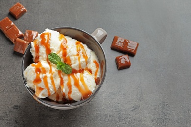 Tasty ice cream with caramel sauce in mug and candies on table