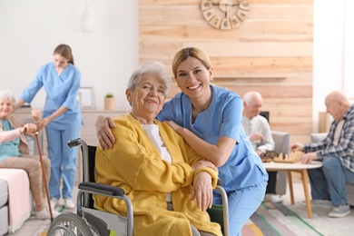 Photo of Nurse with elderly woman in wheelchair at retirement home. Assisting senior people