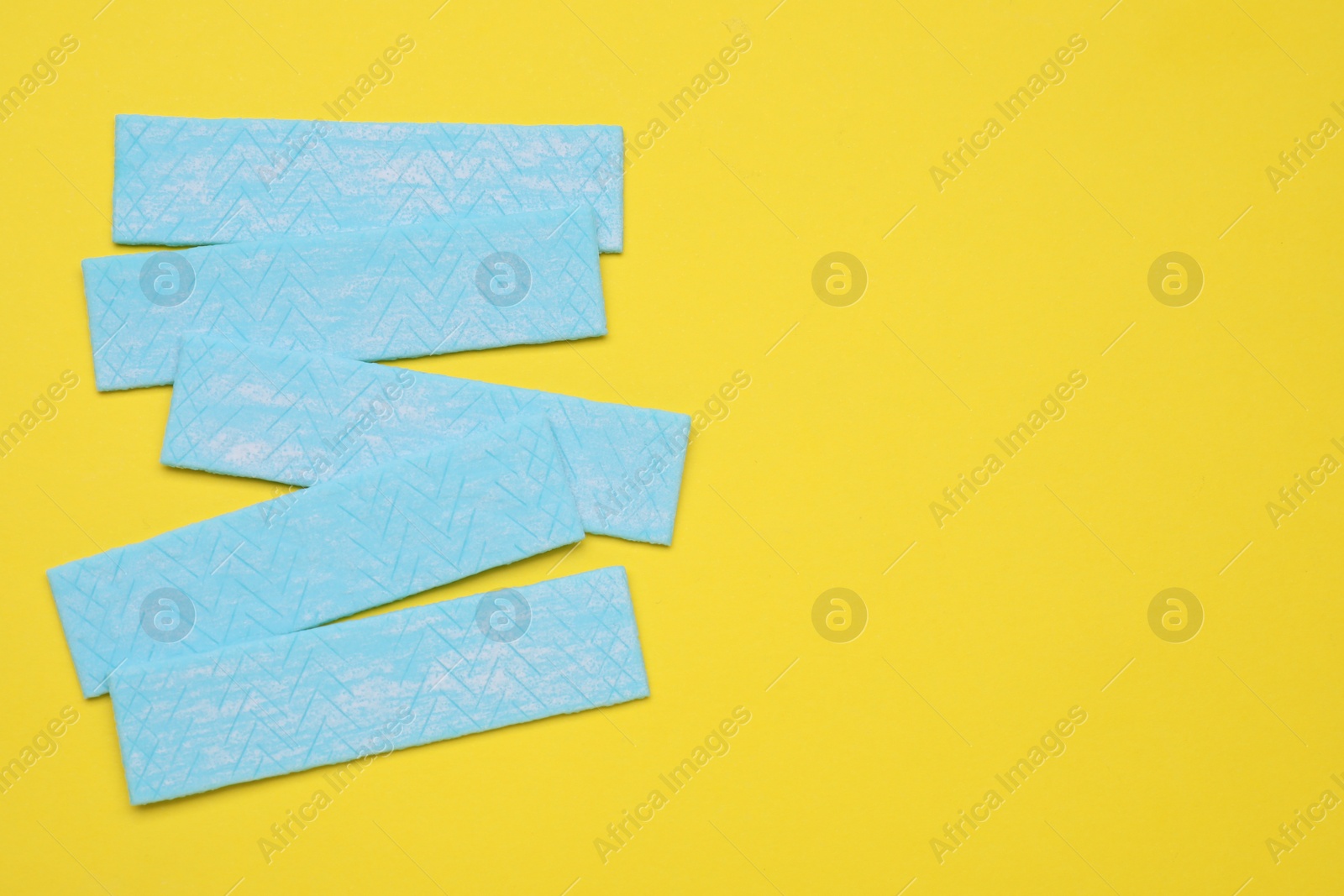 Photo of Many sticks of tasty chewing gum on yellow background, flat lay. Space for text