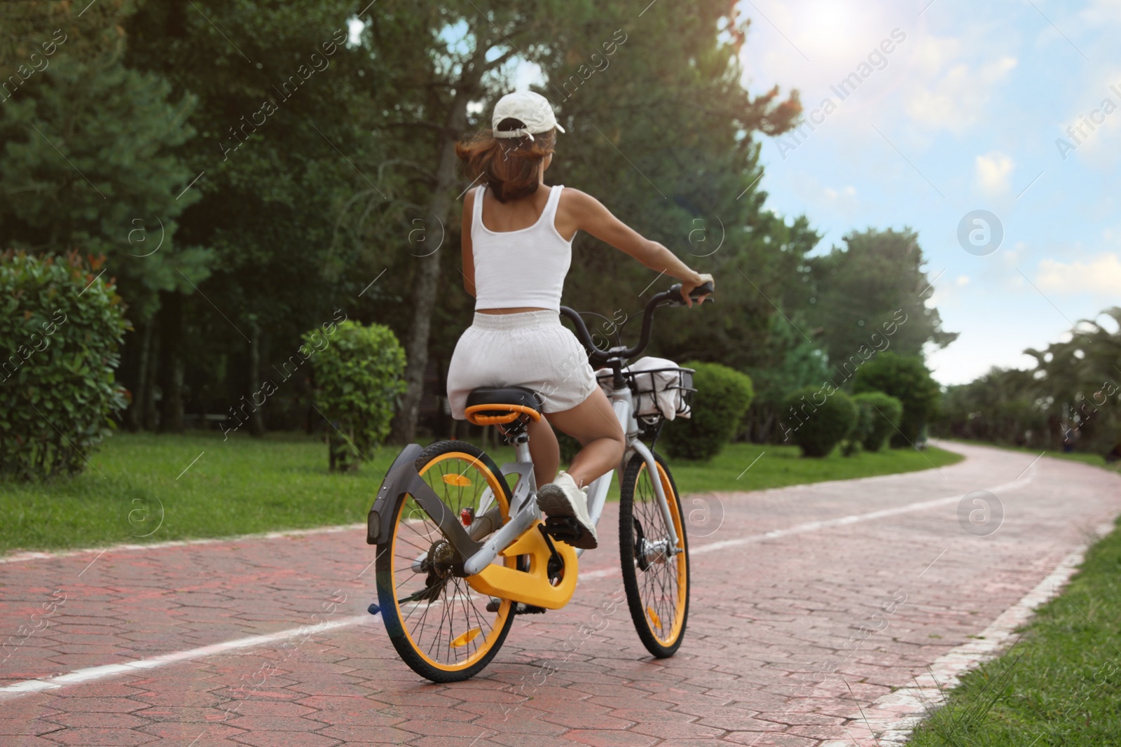 Photo of Young woman riding bicycle on lane outdoors, back view