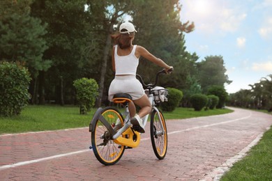 Photo of Young woman riding bicycle on lane outdoors, back view