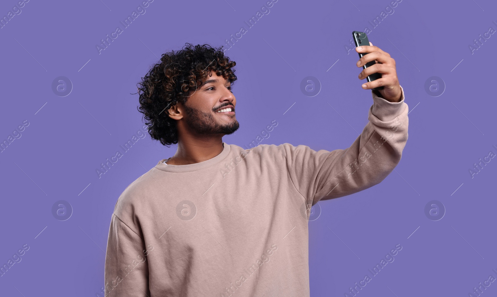 Photo of Handsome smiling man taking selfie with smartphone on violet background, space for text