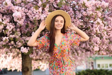 Photo of Beautiful woman in straw hat near blossoming tree on spring day