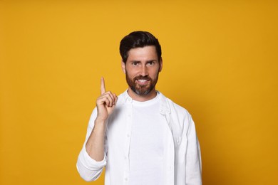Photo of Smiling bearded man pointing index finger up on orange background