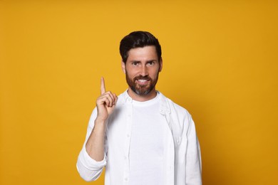 Smiling bearded man pointing index finger up on orange background