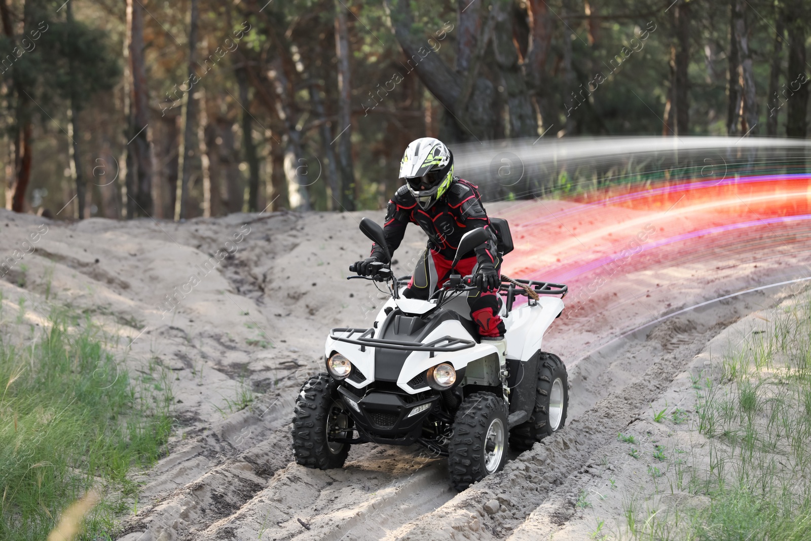 Image of Man driving modern quad bike on sandy road near forest. Light trails showing his speed