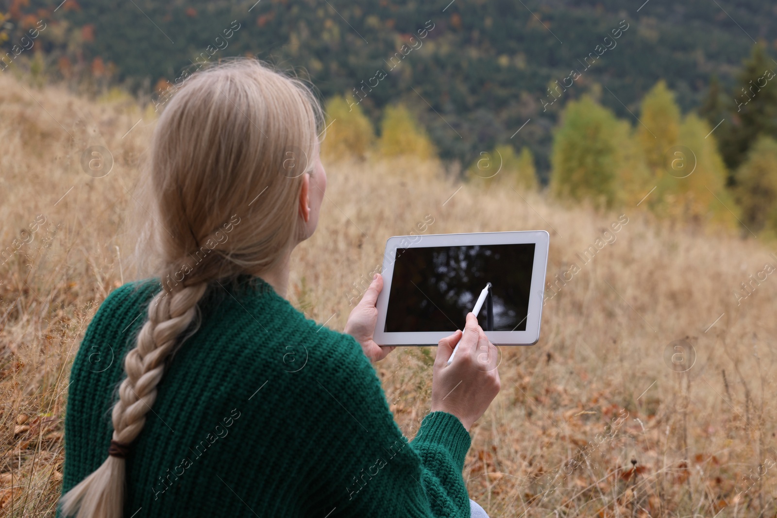 Photo of Young woman drawing on tablet outdoors, back view