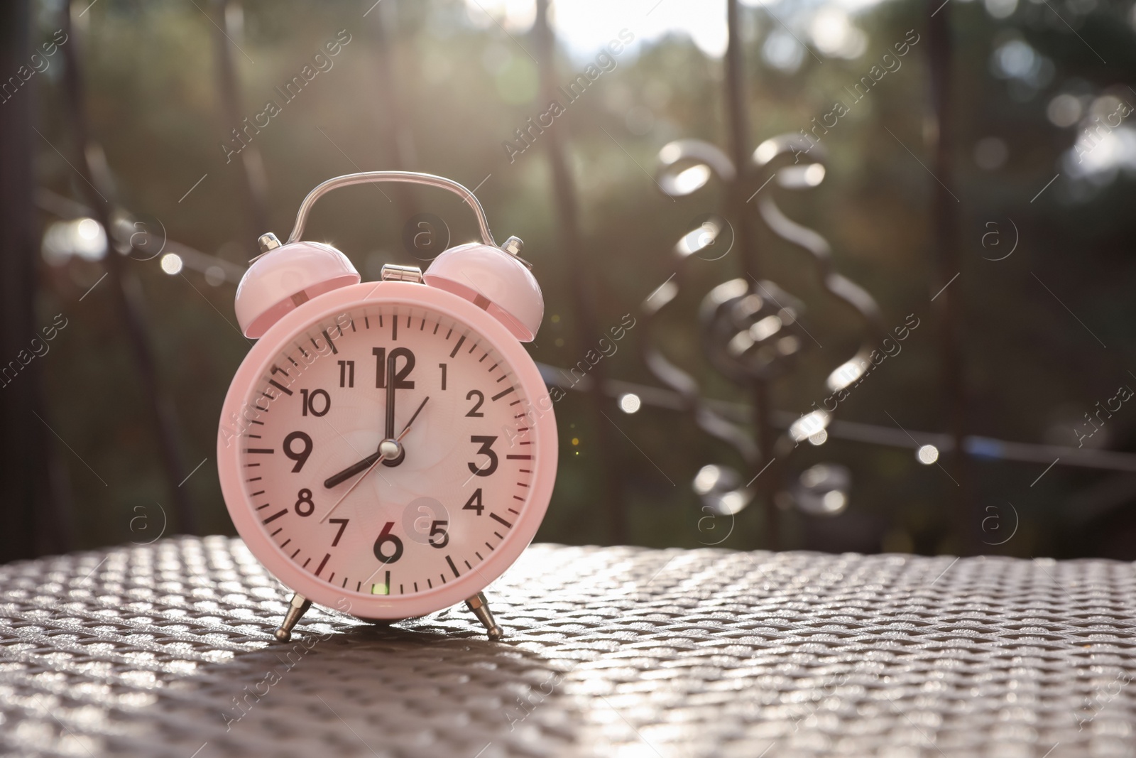 Photo of Pink alarm clock on table outdoors at sunny morning. Space for text