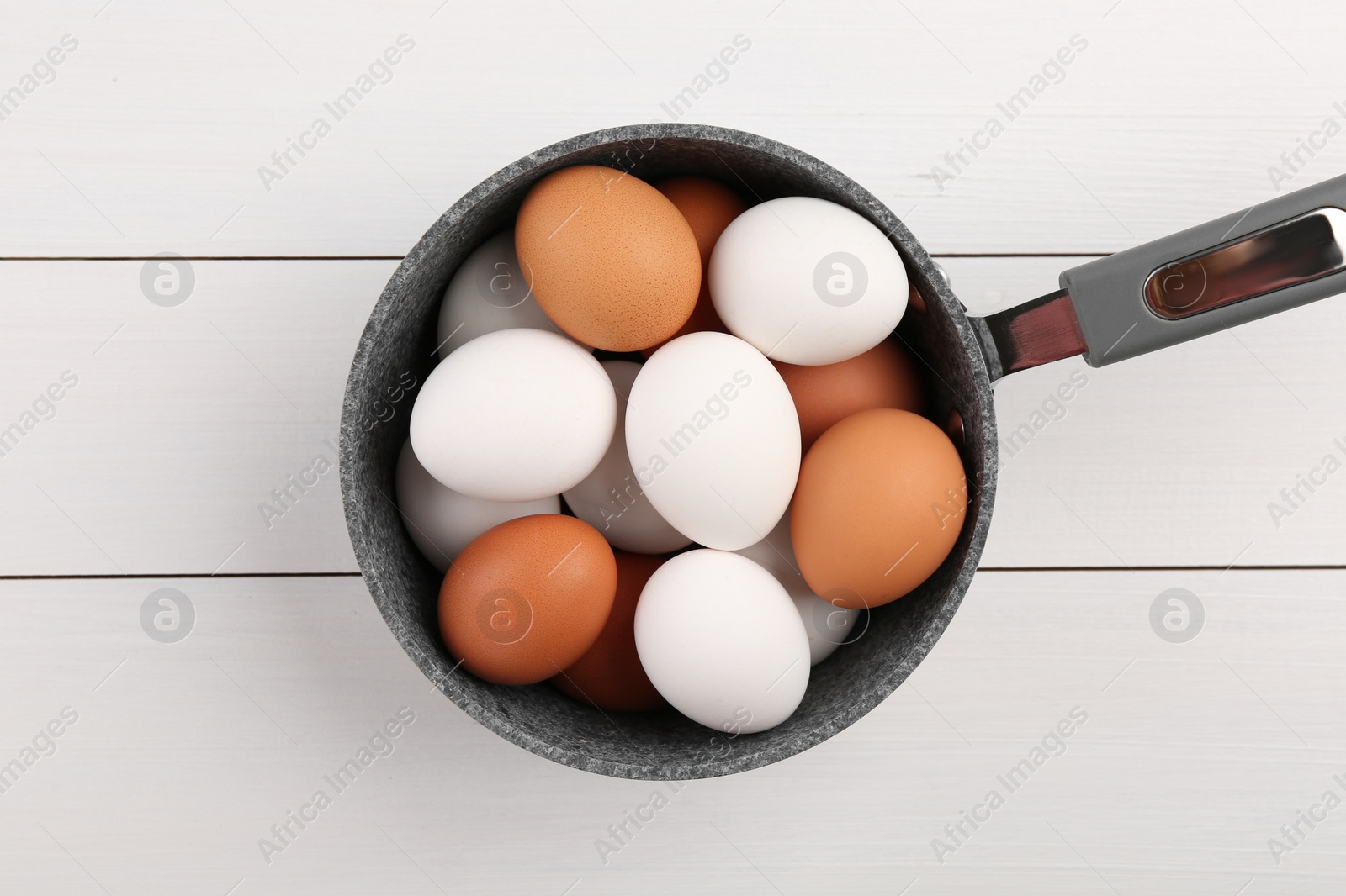 Photo of Unpeeled boiled eggs in saucepan on white wooden table, top view