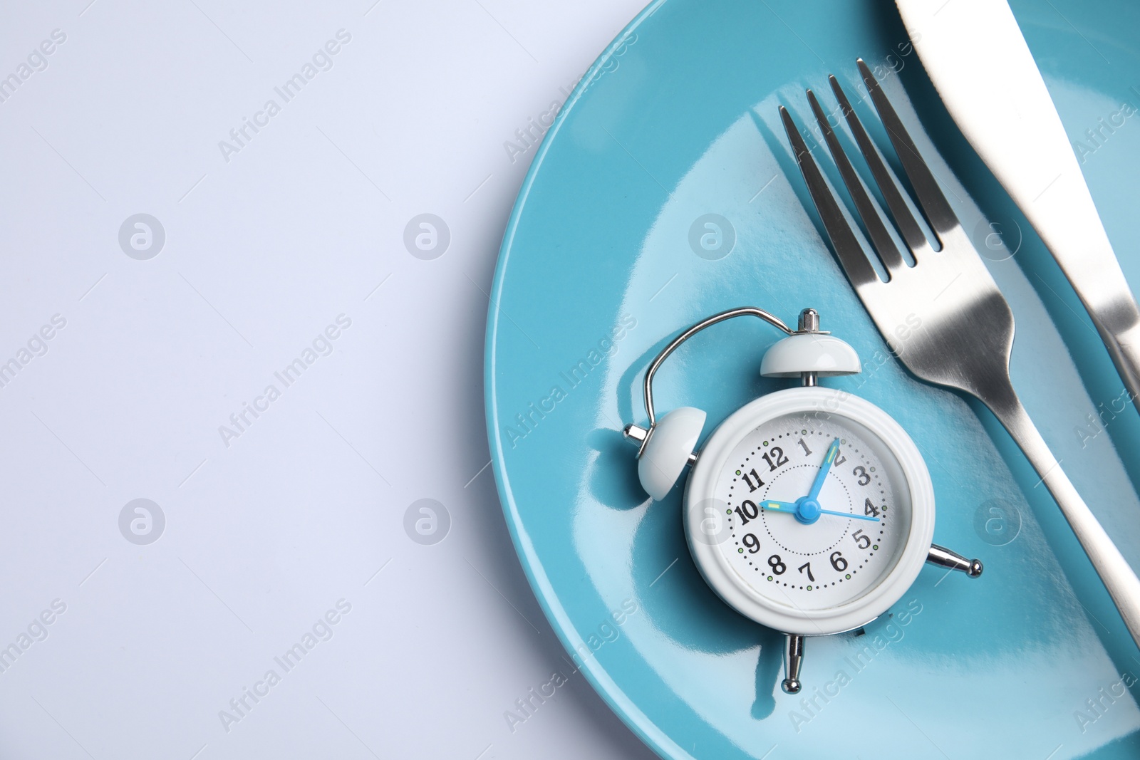 Photo of Alarm clock, plate and cutlery on white background, top view. Diet regime