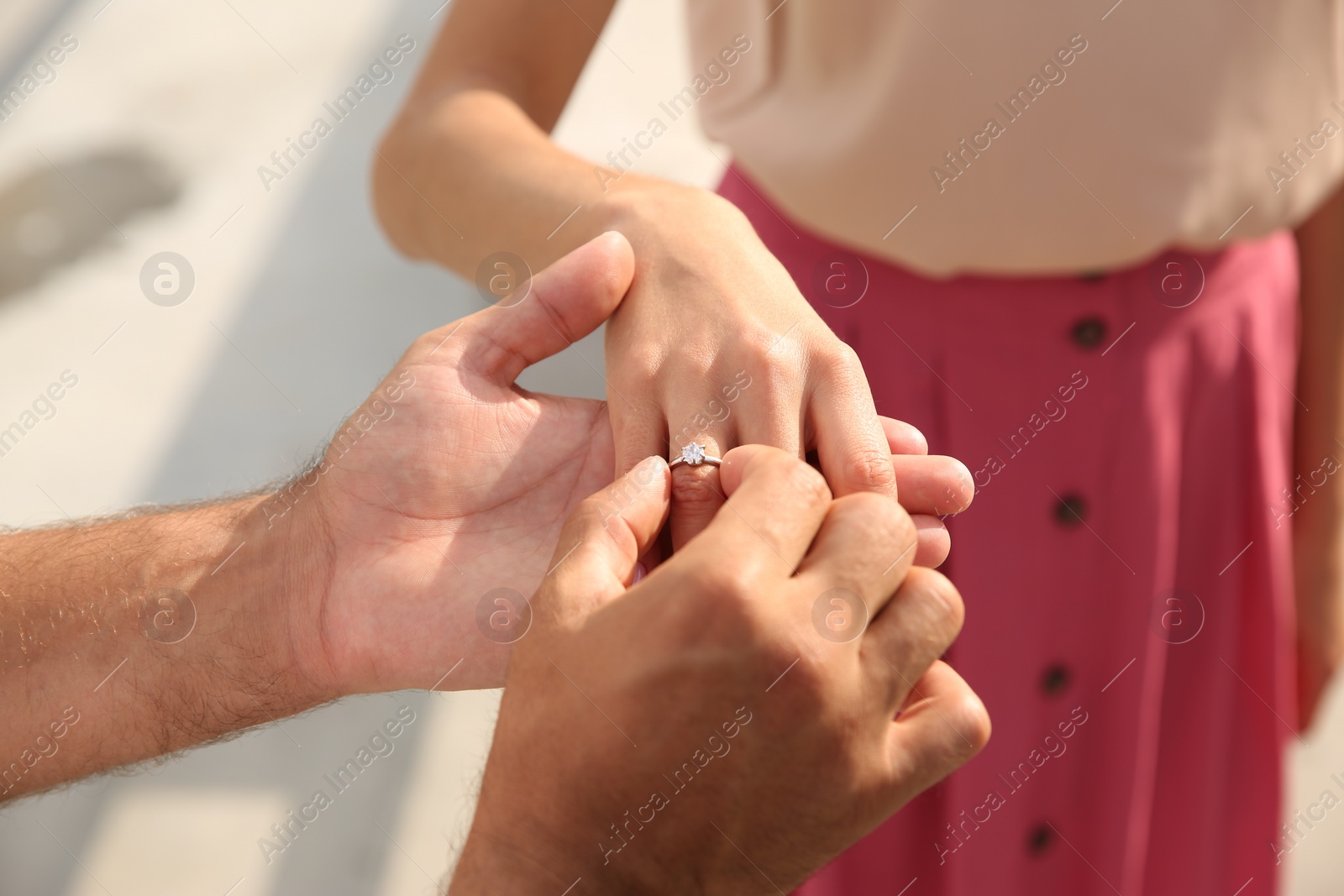 Photo of Man putting engagement ring on his girlfriend's finger outdoors, closeup