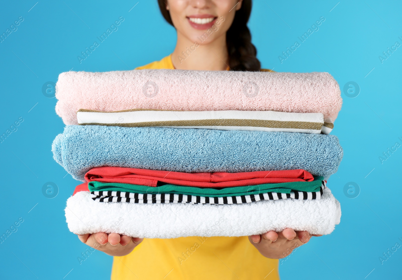 Photo of Young woman holding clean laundry on color background, closeup