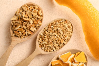 Photo of Spoons with dried orange seasoning zest and peel on beige textured table, flat lay