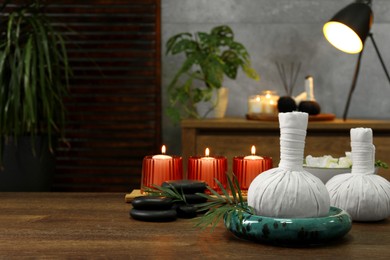 Herbal massage bags, burning candles and spa stones on wooden table indoors, space for text