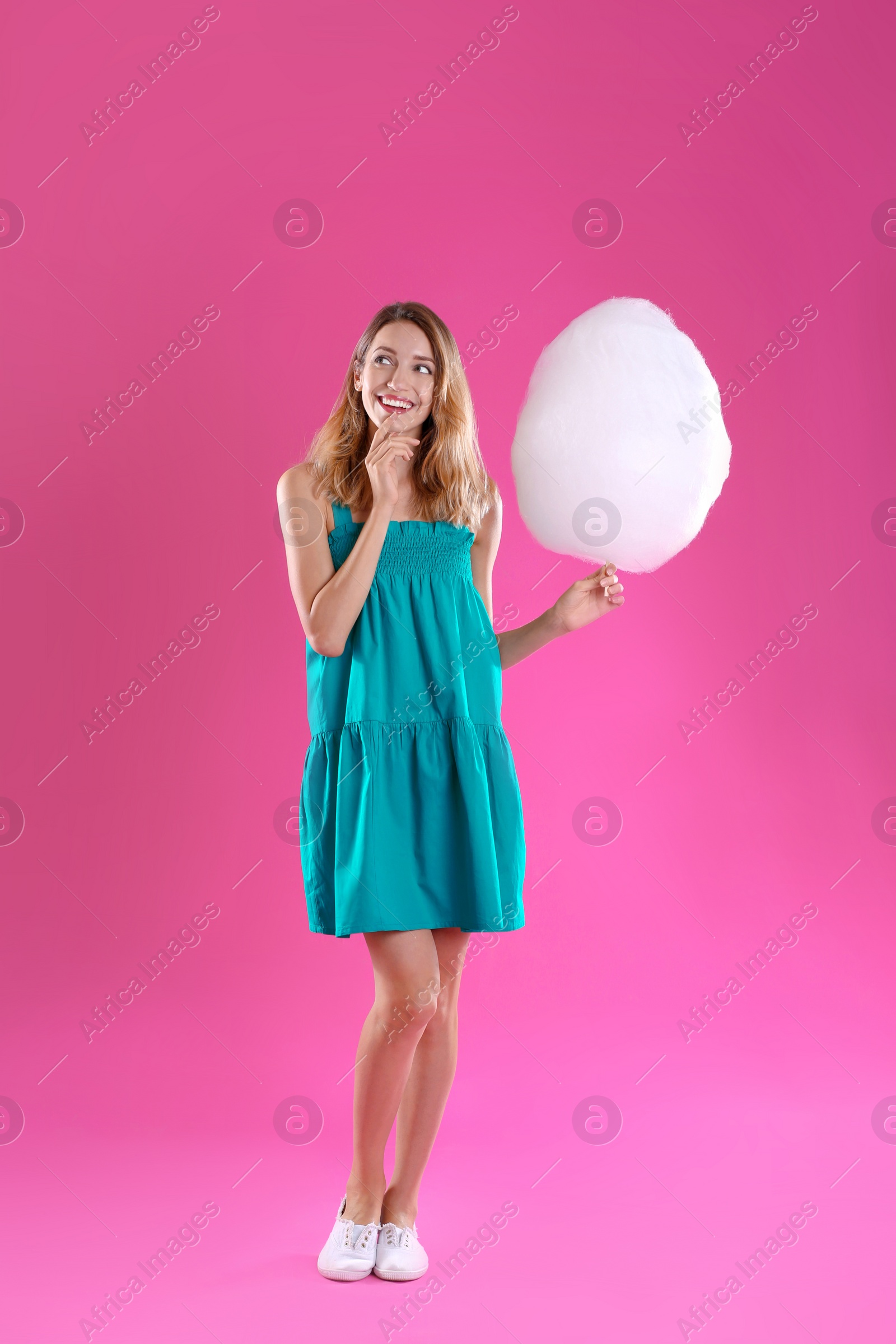 Photo of Happy young woman with cotton candy on pink background