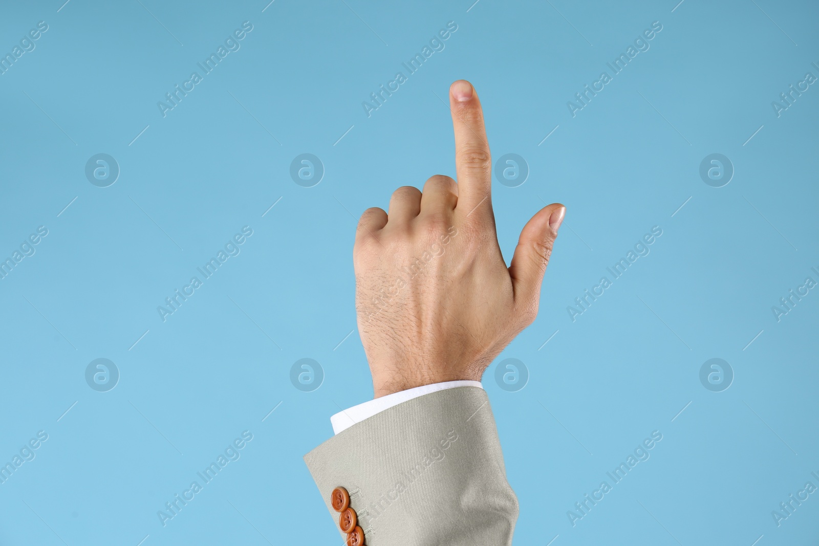Photo of Businessman pointing at something on light blue background, closeup. Finger gesture