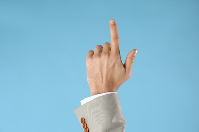 Businessman pointing at something on light blue background, closeup. Finger gesture