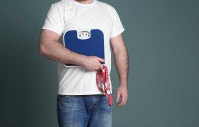 Photo of Overweight man with scale and measuring tape on color background