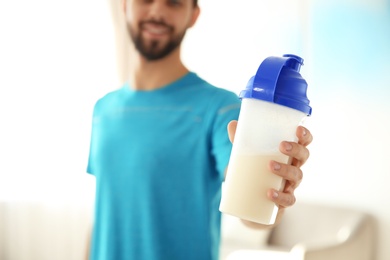Young man with bottle of protein shake at home, closeup