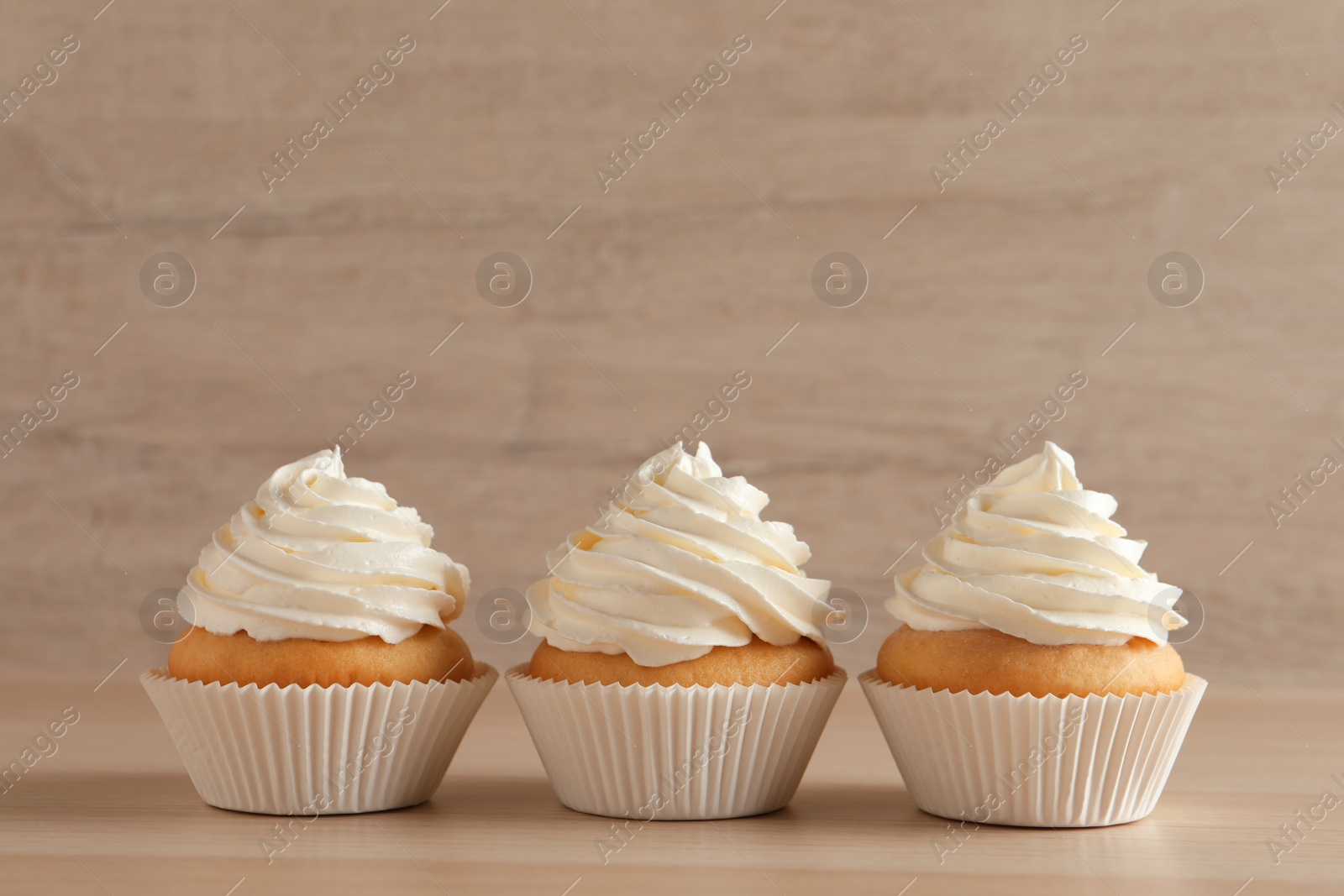 Photo of Delicious cupcakes with white cream on wooden table